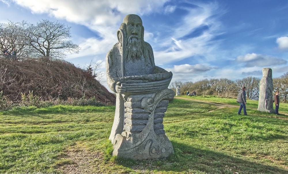 a statue of a man sitting on top of a grass covered field