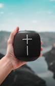 a hand holding a black speaker with a cross on it