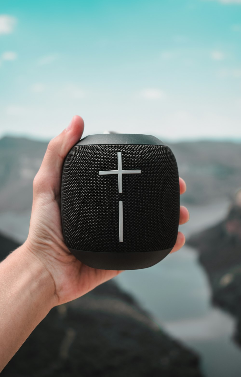 a hand holding a black speaker with a cross on it