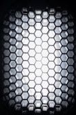 A close-up view of a hexagonal grid pattern made of a dark material, with light shining through from behind, creating a glowing effect.