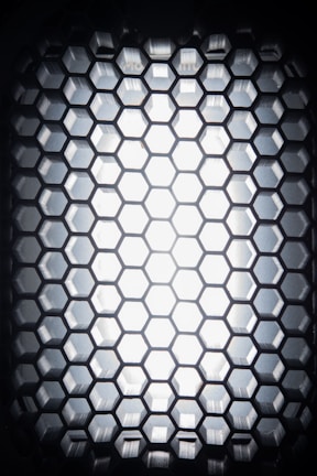A close-up view of a hexagonal grid pattern made of a dark material, with light shining through from behind, creating a glowing effect.