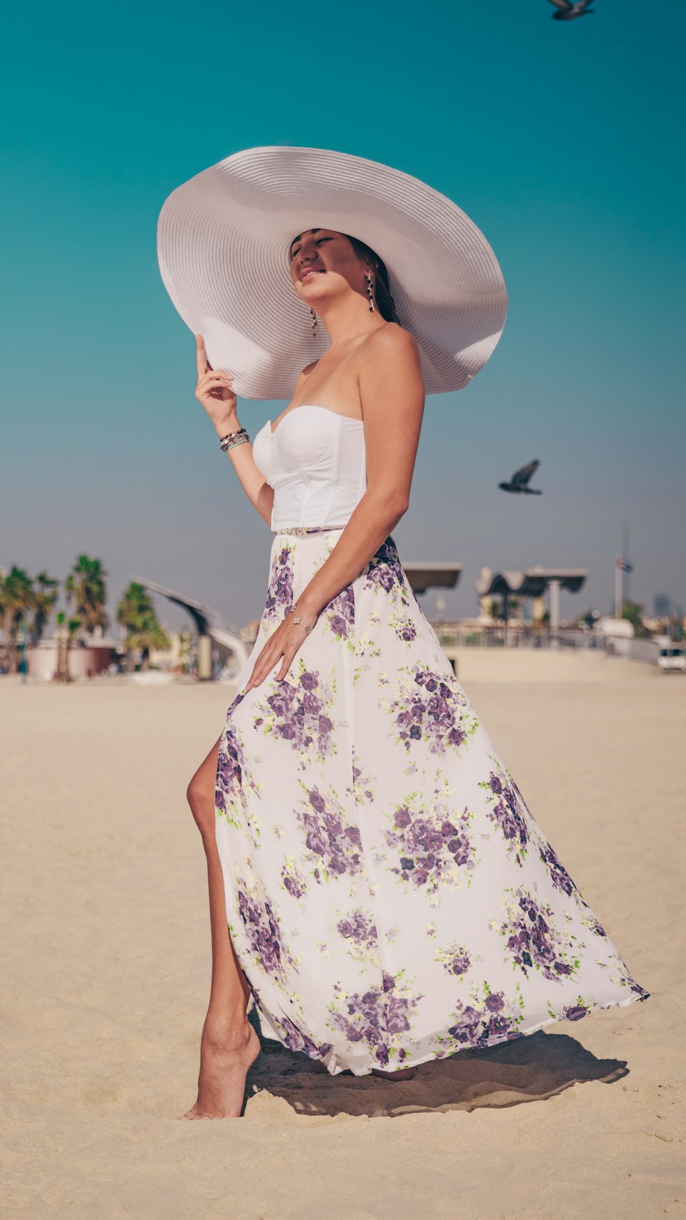 a woman in a white hat and dress on the beach