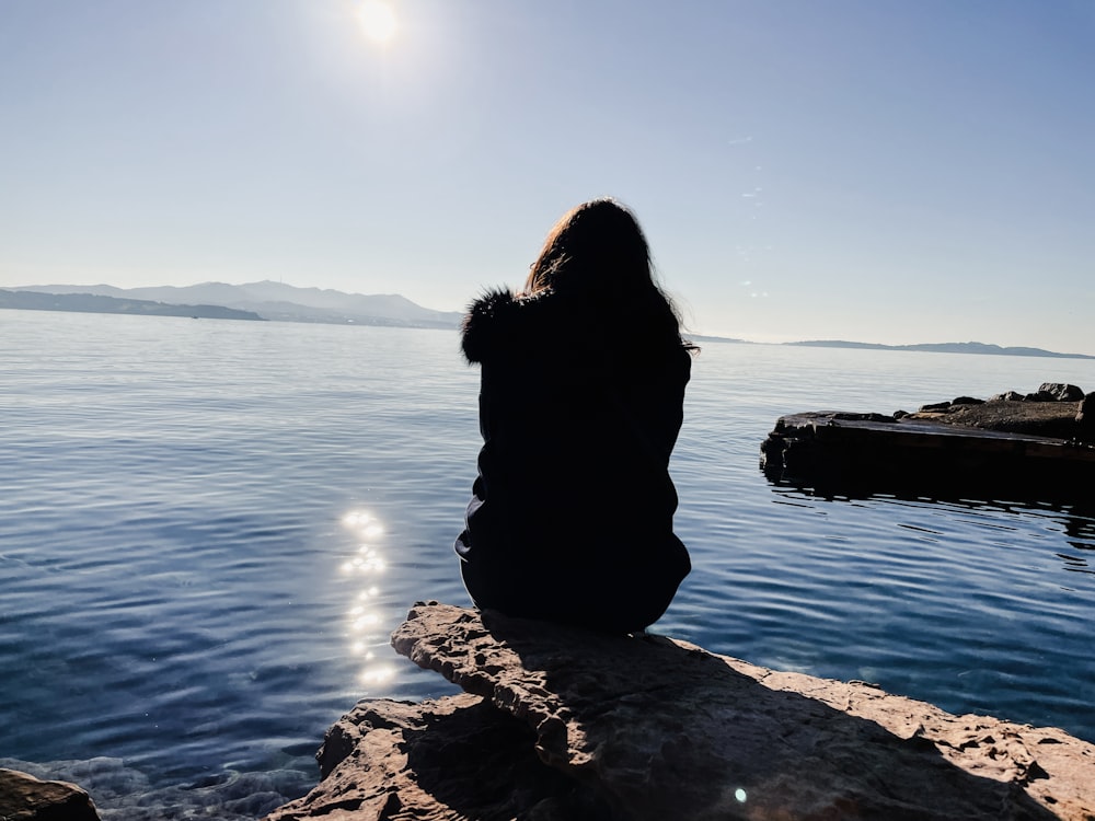a person sitting on a rock looking out at the water