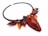 An intricately designed necklace featuring a large teardrop-shaped gemstone in a deep reddish hue. The necklace is adorned with beads in shades of black, red, and orange, arranged in a pattern that resembles leaves and abstract shapes. The craftsmanship is detailed and artistic, highlighting a blend of smooth and textured surfaces.