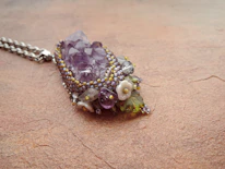 A handcrafted golden orchid pendant resting on a rich purple velvet cloth.