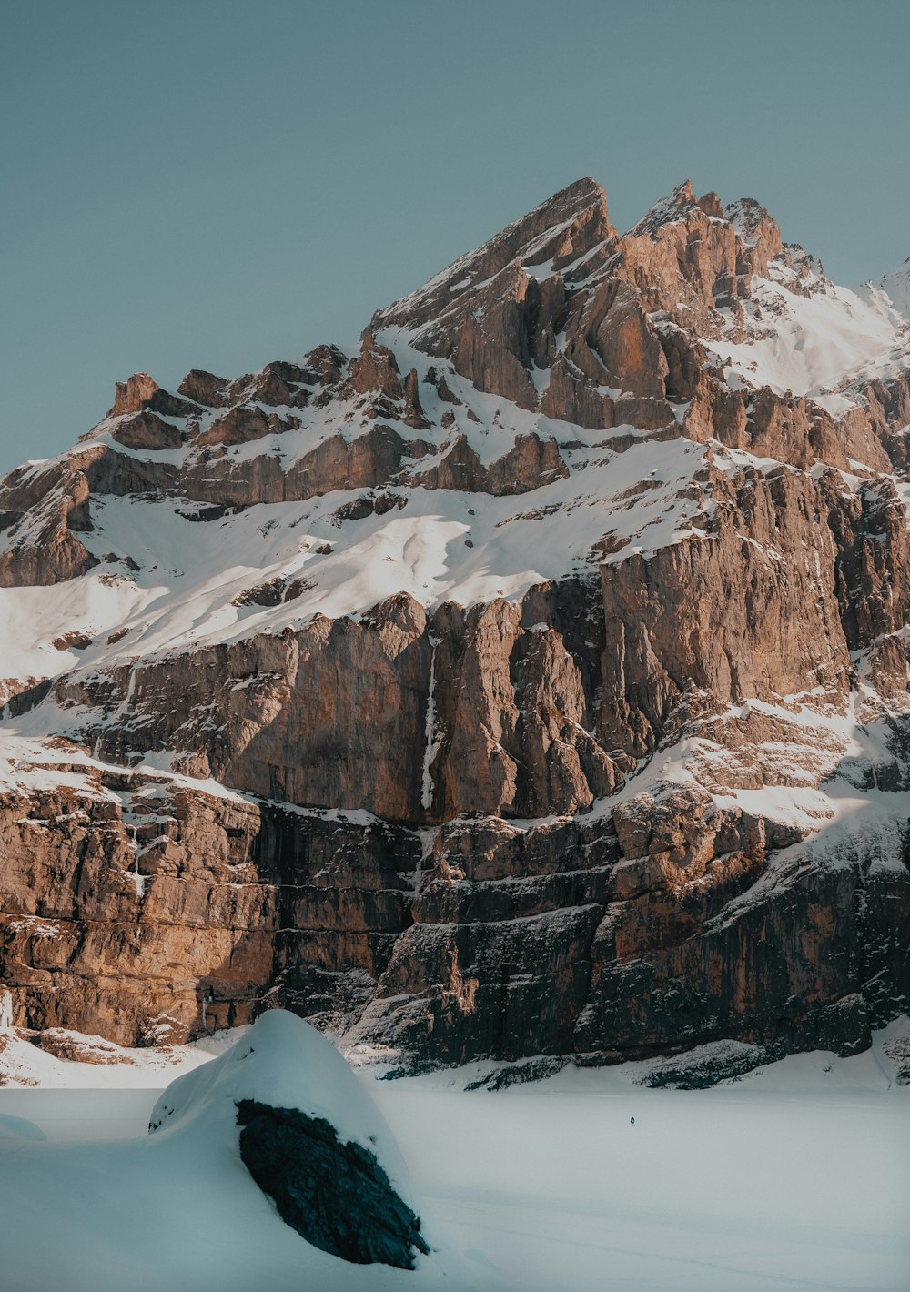 a snow covered mountain with a large rock in the foreground