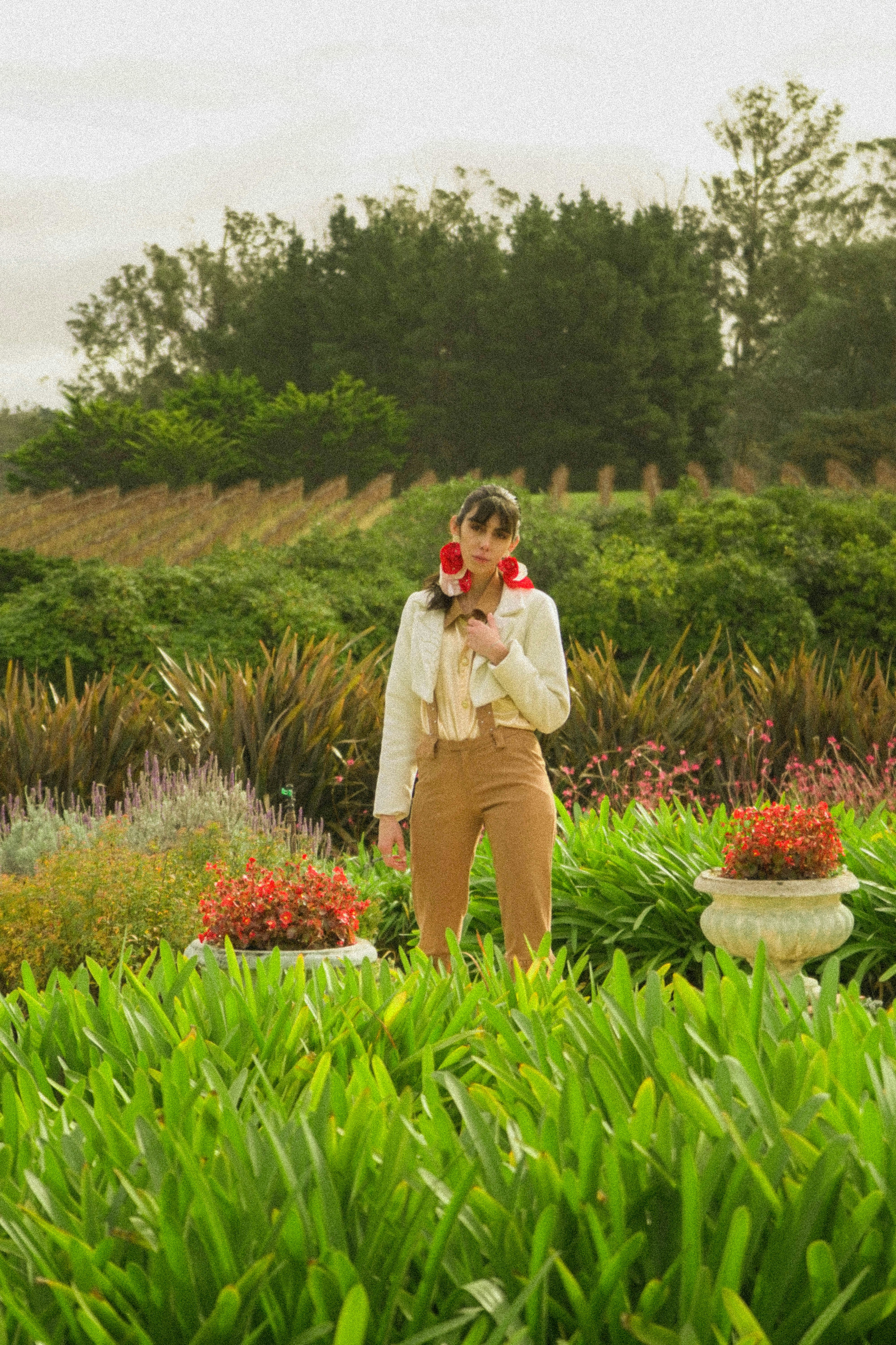 a woman standing in a garden holding a red flower
