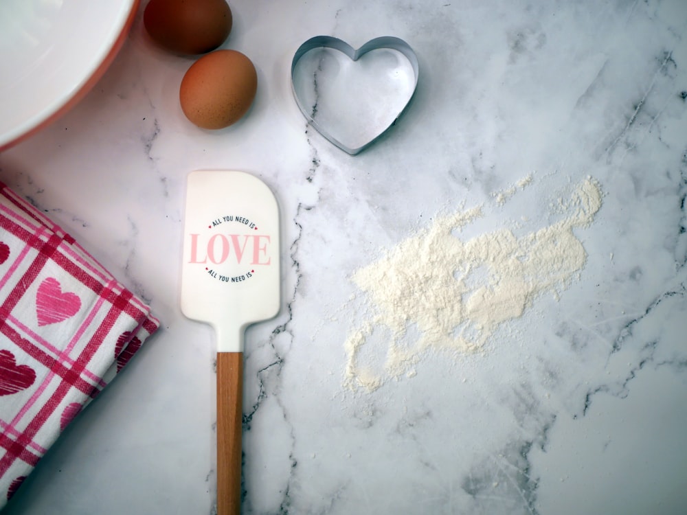 a heart shaped cookie cutter next to flour and eggs
