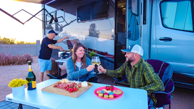 A lively gathering enjoying the Celebration Box, with friends laughing and sharing cheese and accompaniments outdoors.