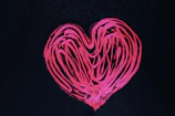 Close-up of hands painting a bright heart symbol on a canvas.