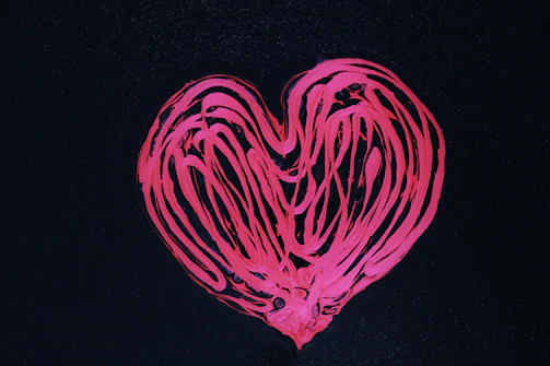 Close-up of hands painting a bright heart symbol on a canvas.