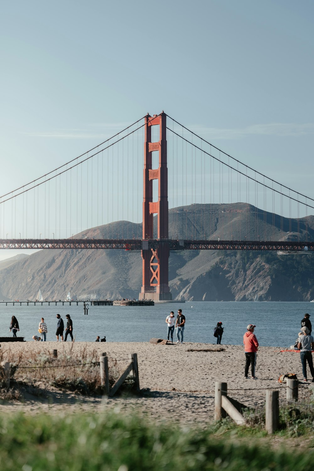 a group of people standing on a beach next to a bridge