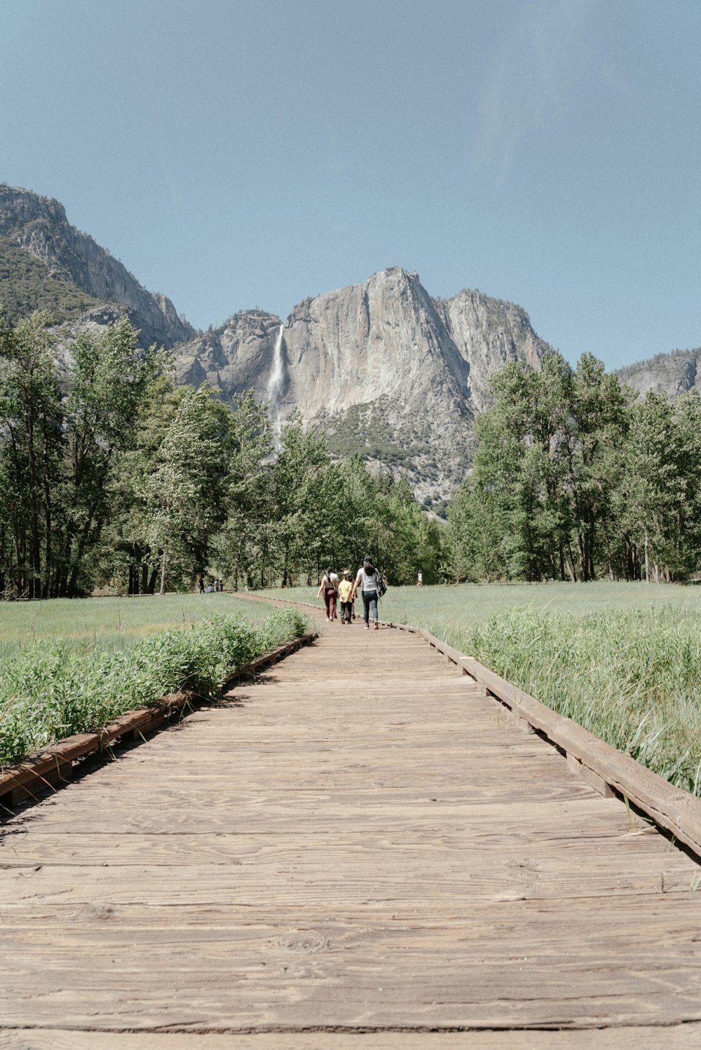 three people walking down a wooden path in the mountains