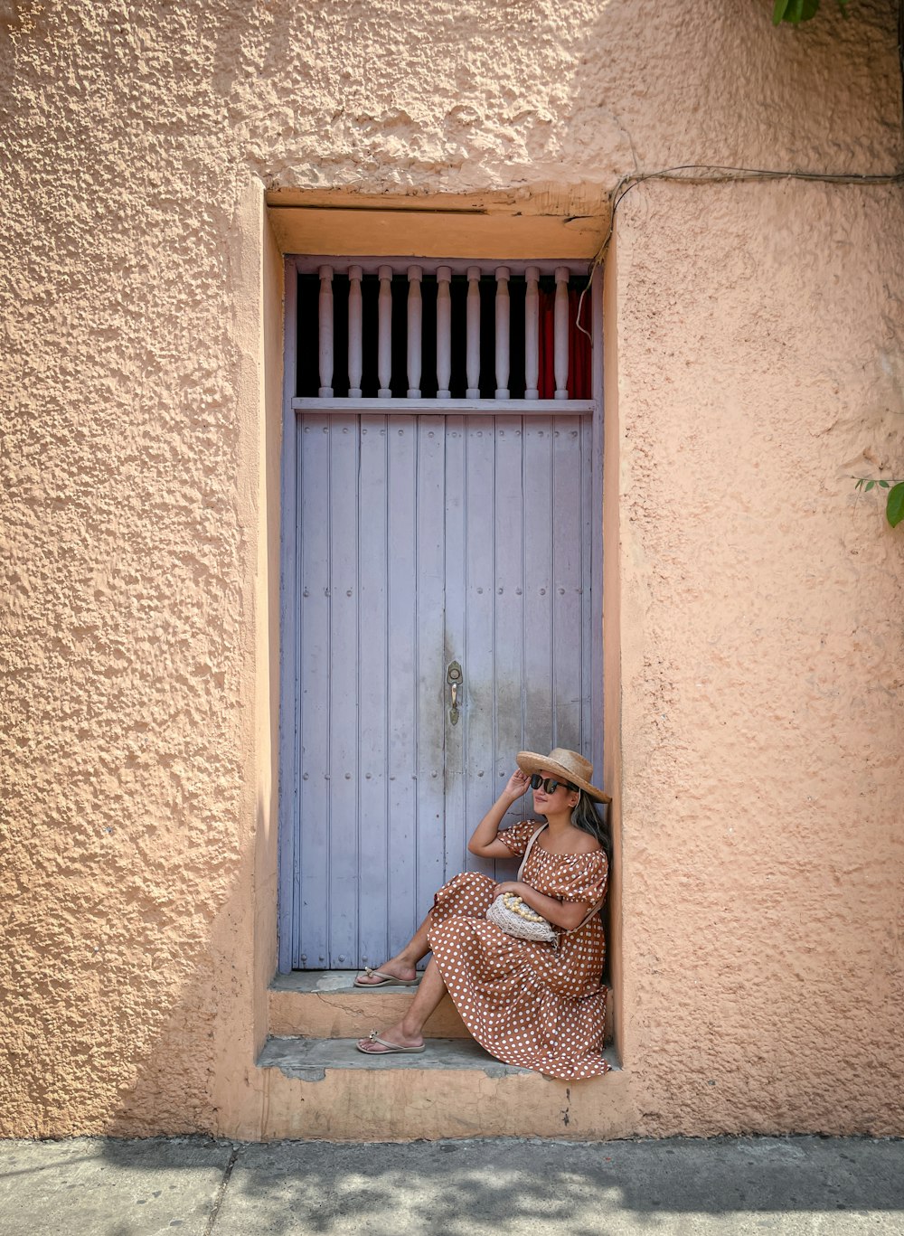 Una mujer con un vestido y un sombrero sentada en una ventana