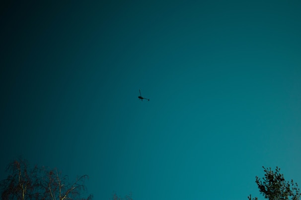 An ominous black helicopter hovering silently over a dark forest under a moonlit sky, casting eerie shadows below.
