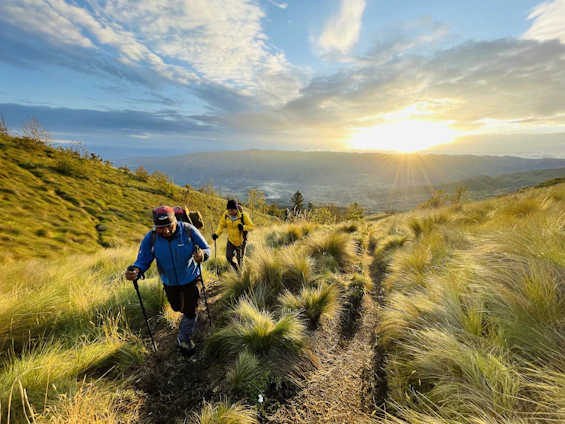 A hiker wearing a sleek hypershell exoskeleton walking confidently on a scenic mountain trail under a golden sunset.