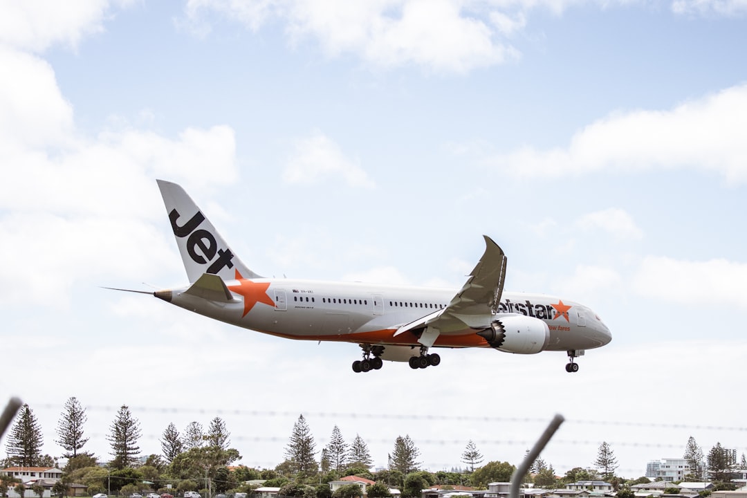 a large jetliner flying through a blue cloudy sky, Gold Coast Airport by Josh Withers