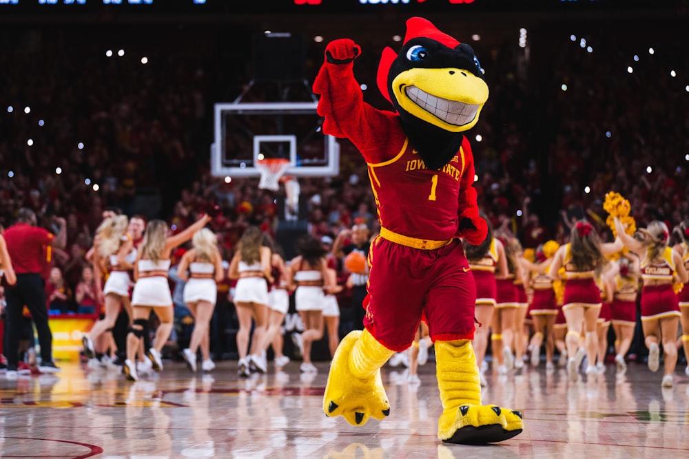 a mascot in a red and yellow outfit dancing on a basketball court