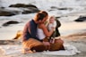 a man and woman sitting on a beach with a baby