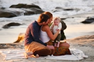 a man and woman sitting on a beach with a baby