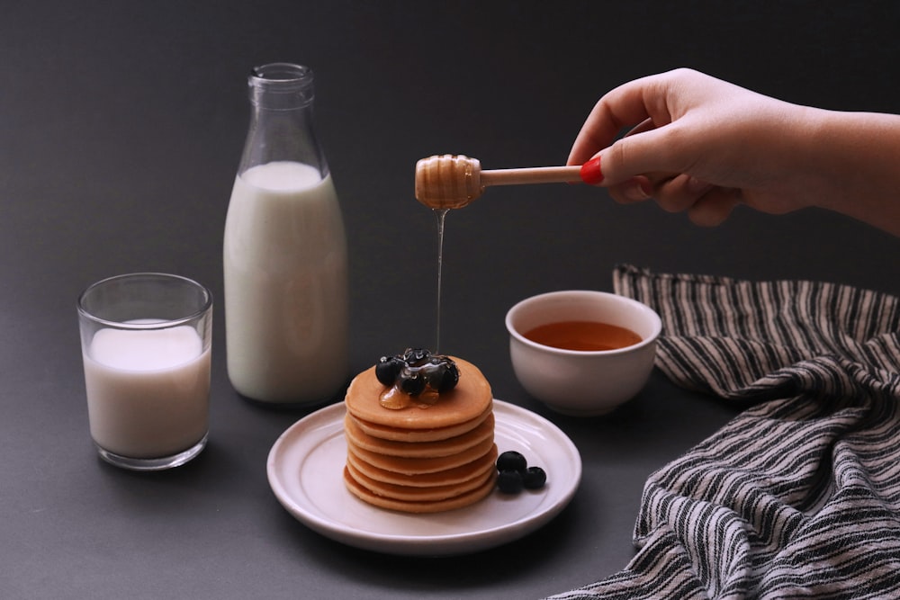 a stack of pancakes on a plate with syrup and a glass of milk