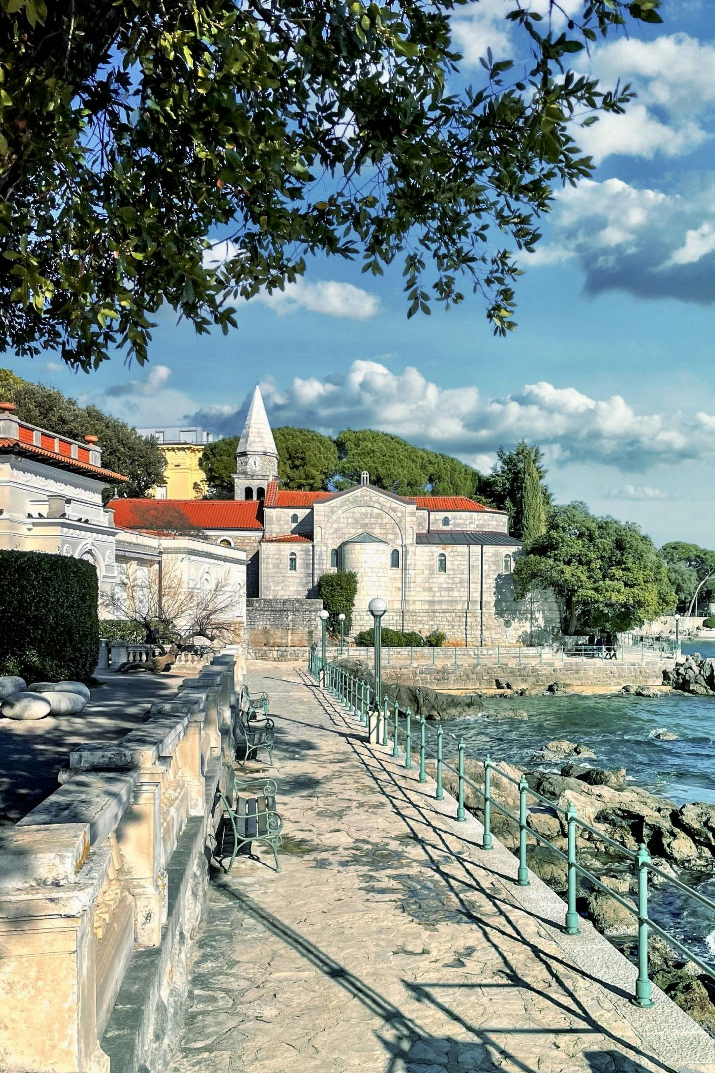 A historic stone church sits along a rocky coastline path.