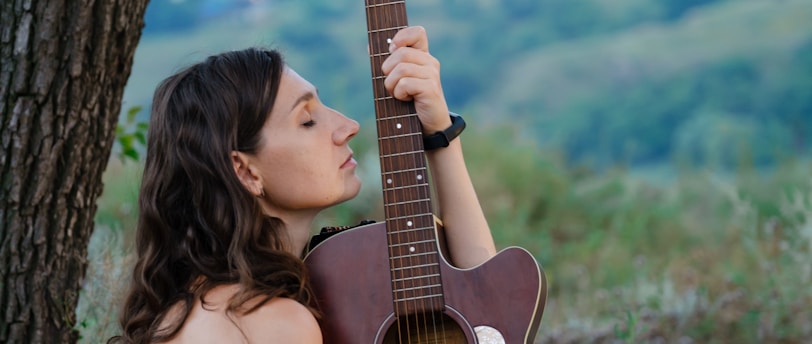 a woman holding a guitar up against a tree