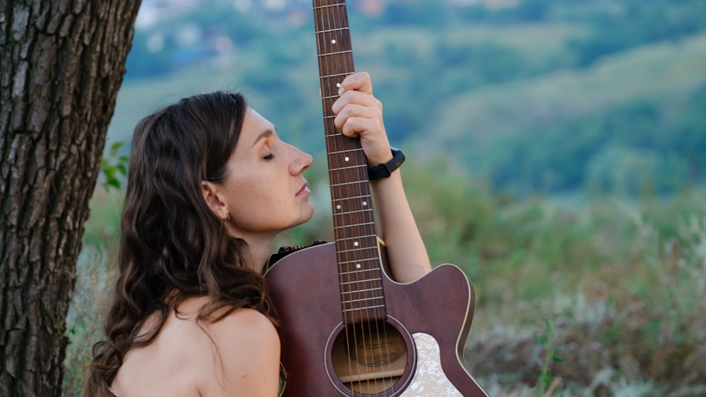 a woman holding a guitar up against a tree