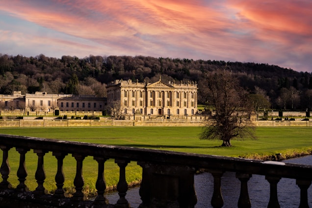 A sweeping view of Baddiley Hall’s grand façade bathed in soft golden light at dusk, framed by manicured gardens.