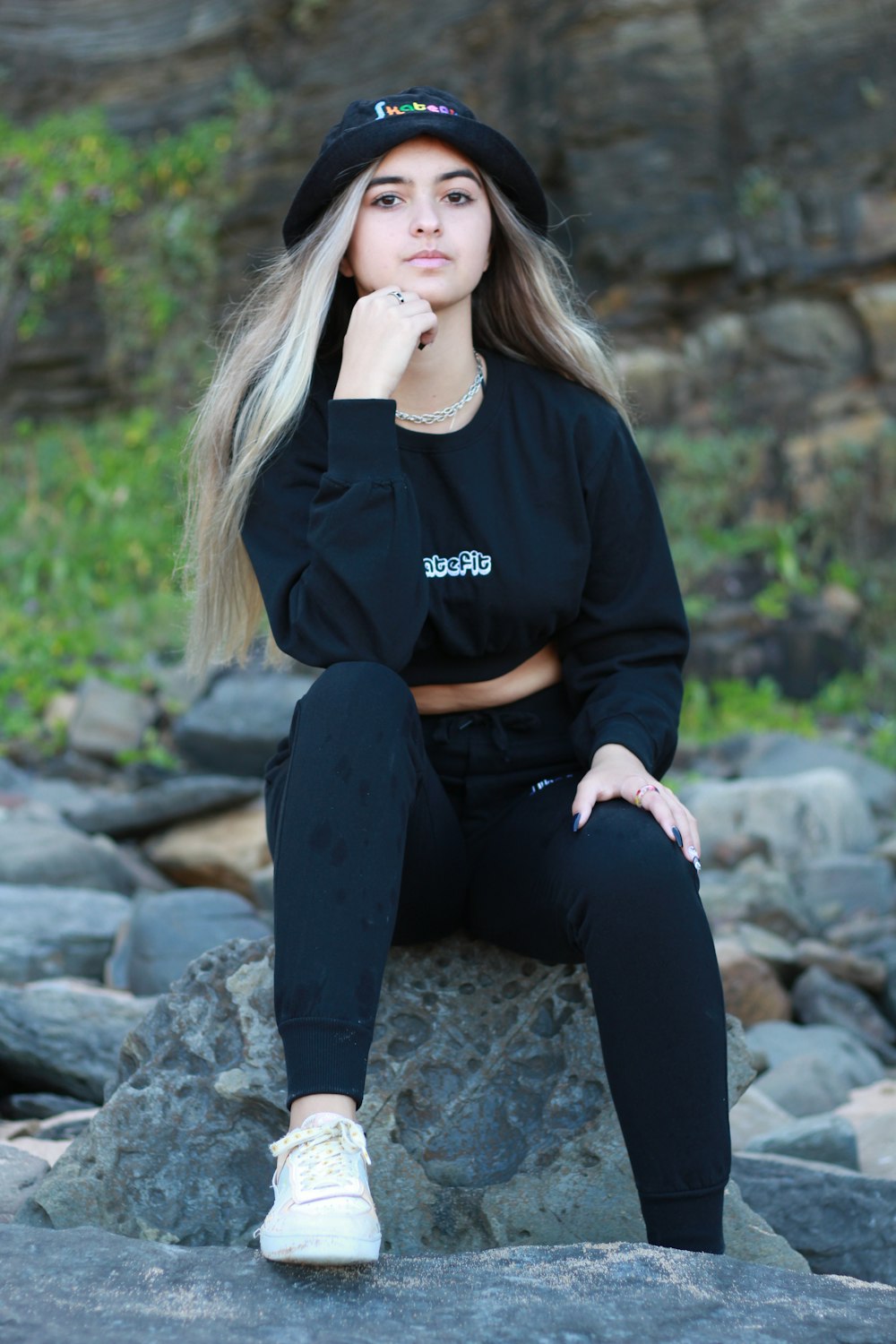 a woman sitting on a rock wearing a black sweatshirt and sweatpants