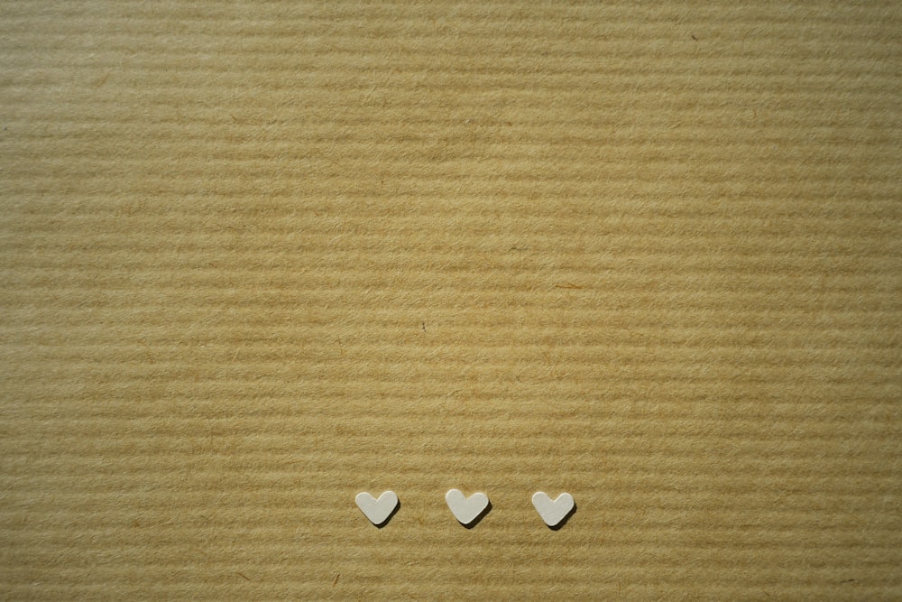 Tres pequeños corazones blancos sobre un fondo de cartón marrón