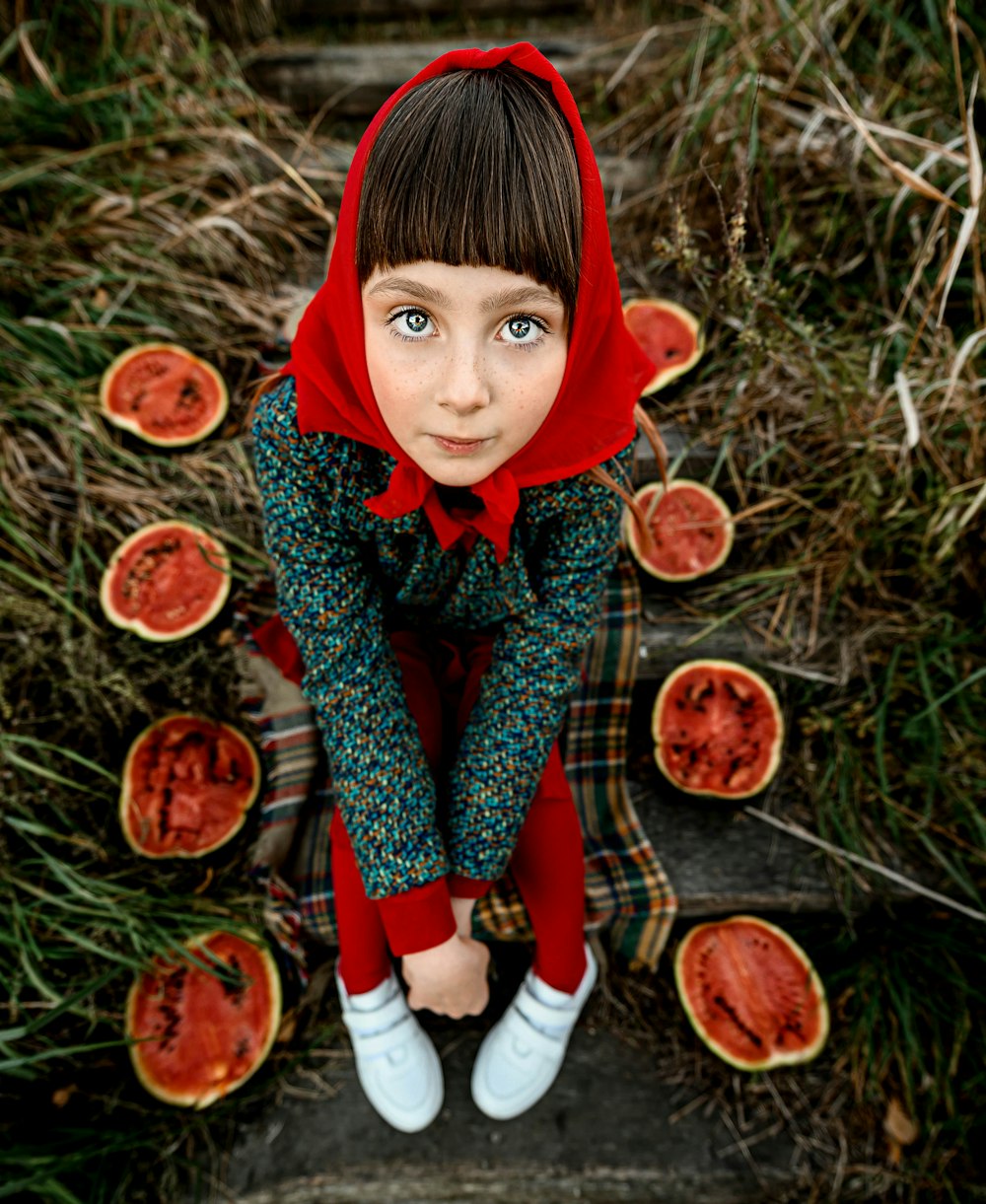 a little girl in a red hoodie is sitting on some slices of watermel