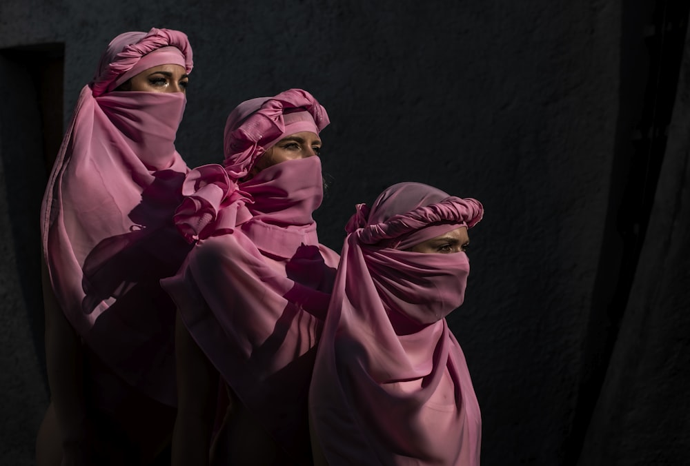 three women in pink headscarves are standing together