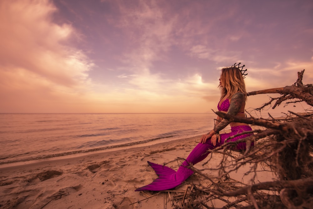 a woman sitting on top of a tree branch on a beach