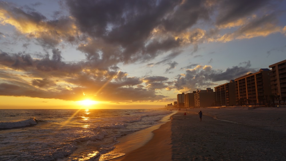 the sun is setting on the beach near a hotel