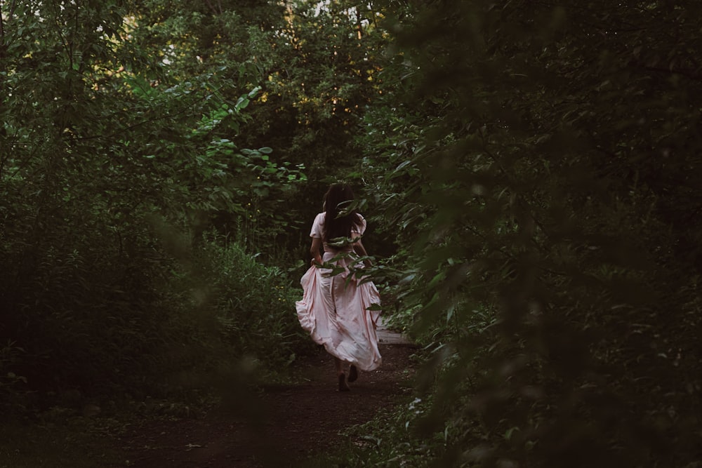 a woman in a white dress is walking through the woods