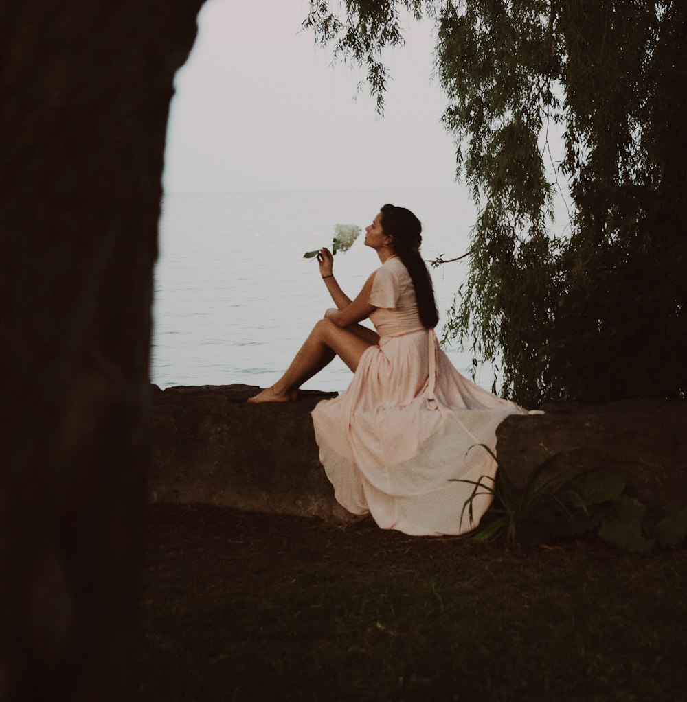 a woman sitting on a rock next to a body of water