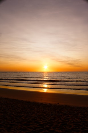 the sun is setting over the ocean on the beach