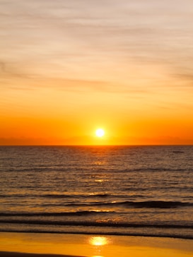the sun is setting over the ocean on the beach