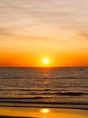 the sun is setting over the ocean on the beach