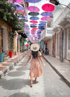 a woman in a dress and hat walking down a street