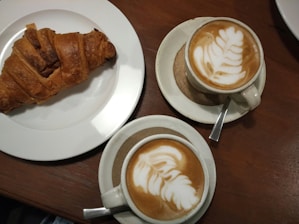 A close-up of a coffee cup and a freshly baked croissant on a wooden table.