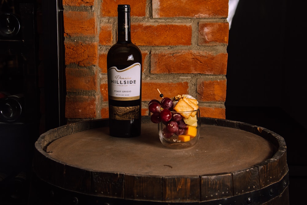 a bottle of wine sitting next to a glass filled with fruit