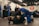 A group of people are practicing Brazilian Jiu-Jitsu in a martial arts gym. Two individuals are actively engaged in grappling on the mats while others observe or participate in the background. Many are wearing blue and black gis, typical attire for this type of martial art. The atmosphere appears focused and disciplined, with a sense of concentration on the training.
