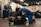 A group of people are practicing Brazilian Jiu-Jitsu in a martial arts gym. Two individuals are actively engaged in grappling on the mats while others observe or participate in the background. Many are wearing blue and black gis, typical attire for this type of martial art. The atmosphere appears focused and disciplined, with a sense of concentration on the training.