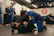 A group of people are practicing Brazilian Jiu-Jitsu in a martial arts gym. Two individuals are actively engaged in grappling on the mats while others observe or participate in the background. Many are wearing blue and black gis, typical attire for this type of martial art. The atmosphere appears focused and disciplined, with a sense of concentration on the training.