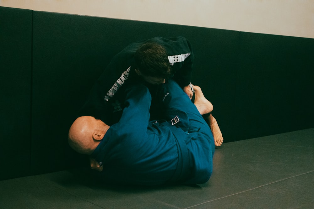a man in a blue shirt is wrestling another man in a black shirt