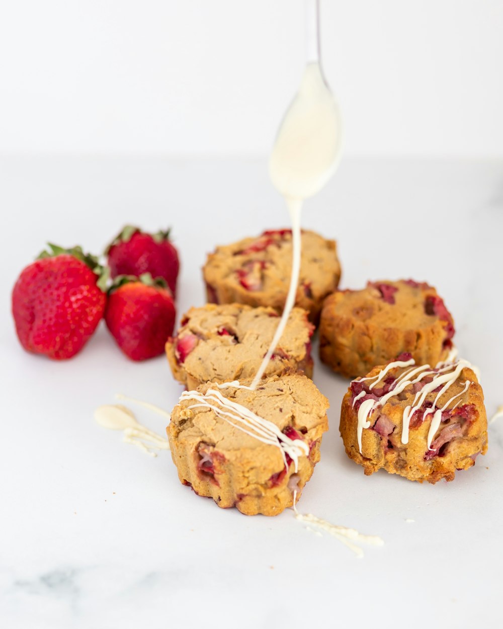 a spoon drizzling white icing onto some strawberry muffins