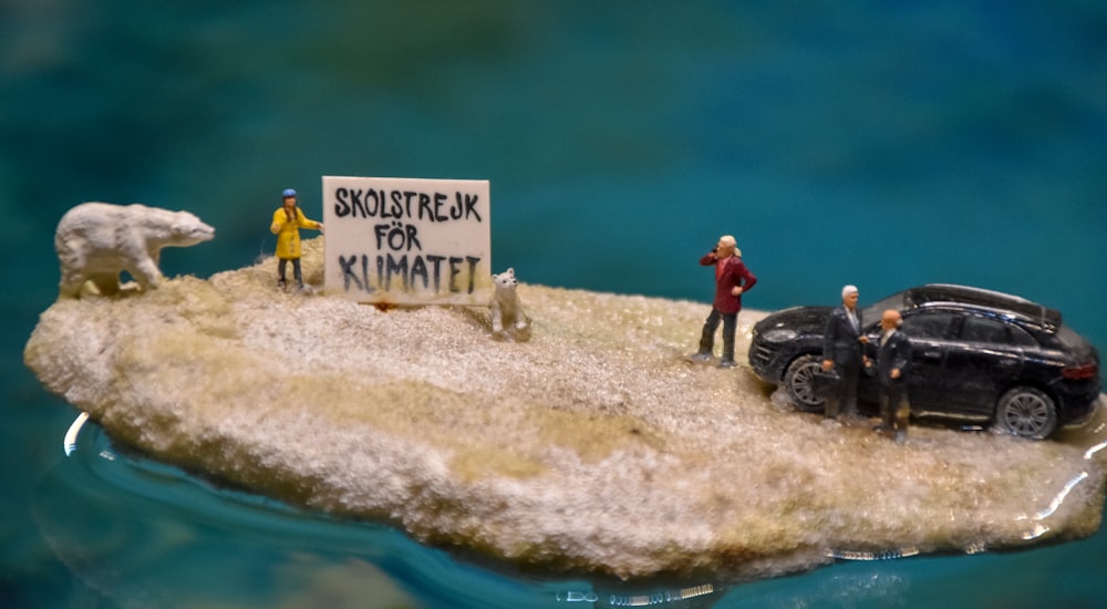 una escena en miniatura de personas de pie en una pequeña isla con un coche y un oso polar