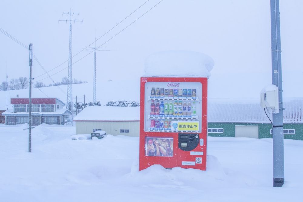 a vending machine covered in snow next to a pole